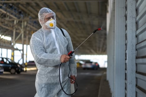 Worker in PPE spraying disinfectant in carpark