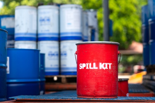 chemical drums on pallets outdoors with a red spill kit bucket