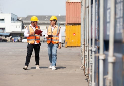 workers with clipboard discussing matters outdoors near freight containers