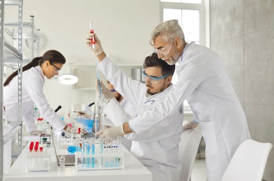 lab worker instructing his fellow to pump chemical liquids into the test tube