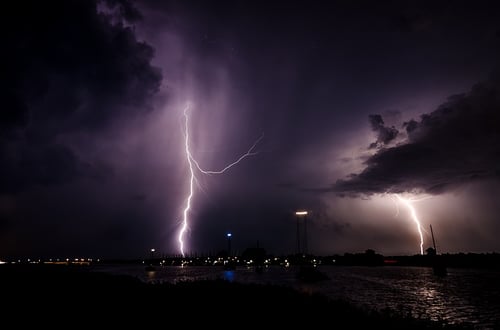 a lighting strike at night, hitting a city located near the water