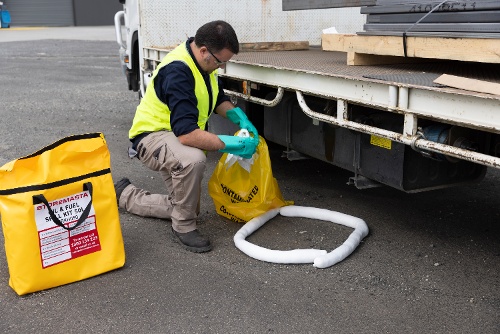 spill kit - worker cleaning up leak from truck with boom and waste bag