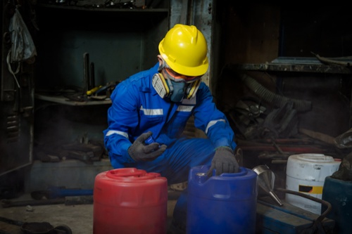 worker in full PPE working with chemical containers