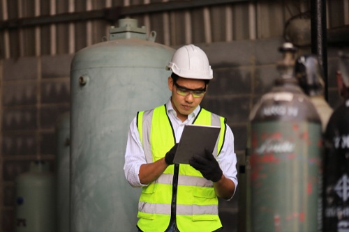 worker looking at checklist in front of large gas cylinders